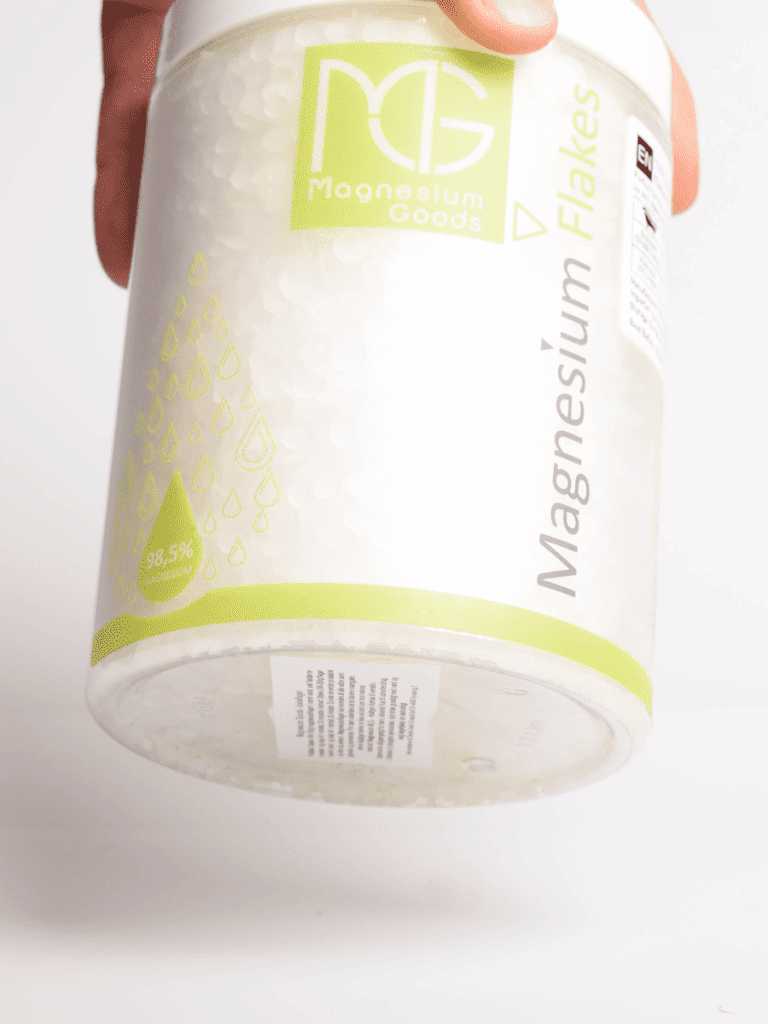 Hand hält Behälter mit Magnesium Flakes von Magnesium Goods, weiße Flocken und grünes Etikett