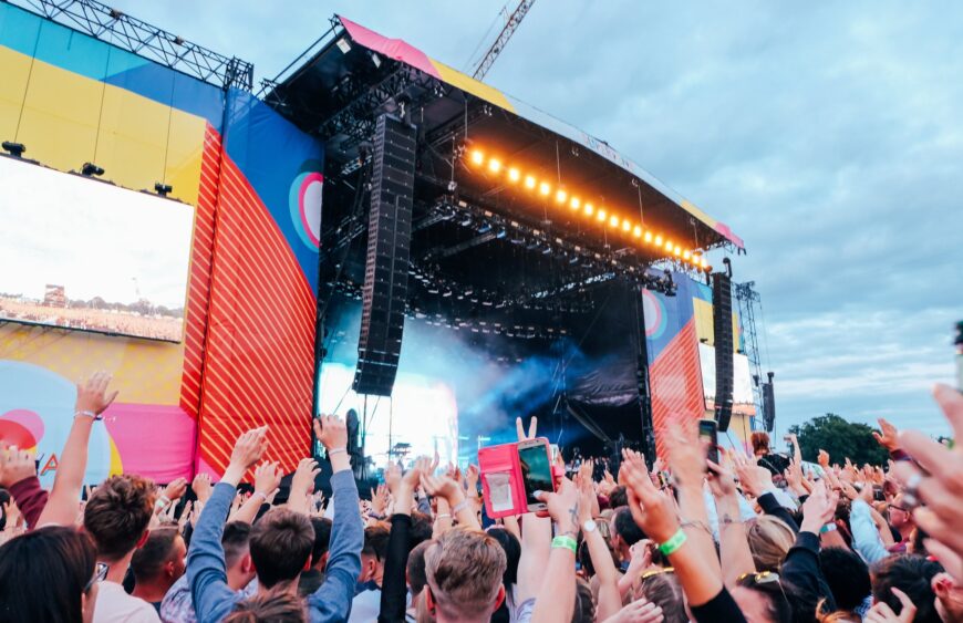 Große Open-Air-Festivalbühne unter Abendhimmel, Publikum mit erhobenen Händen