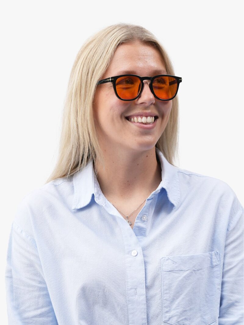 Lächelnde Frau mit langem hellem Haar in hellblauer Bluse, mit orange getönter Brille