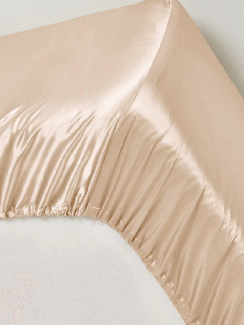 Champagnerfarbenes Satin-Spannbettlaken mit elastischem Rand auf der Matratze