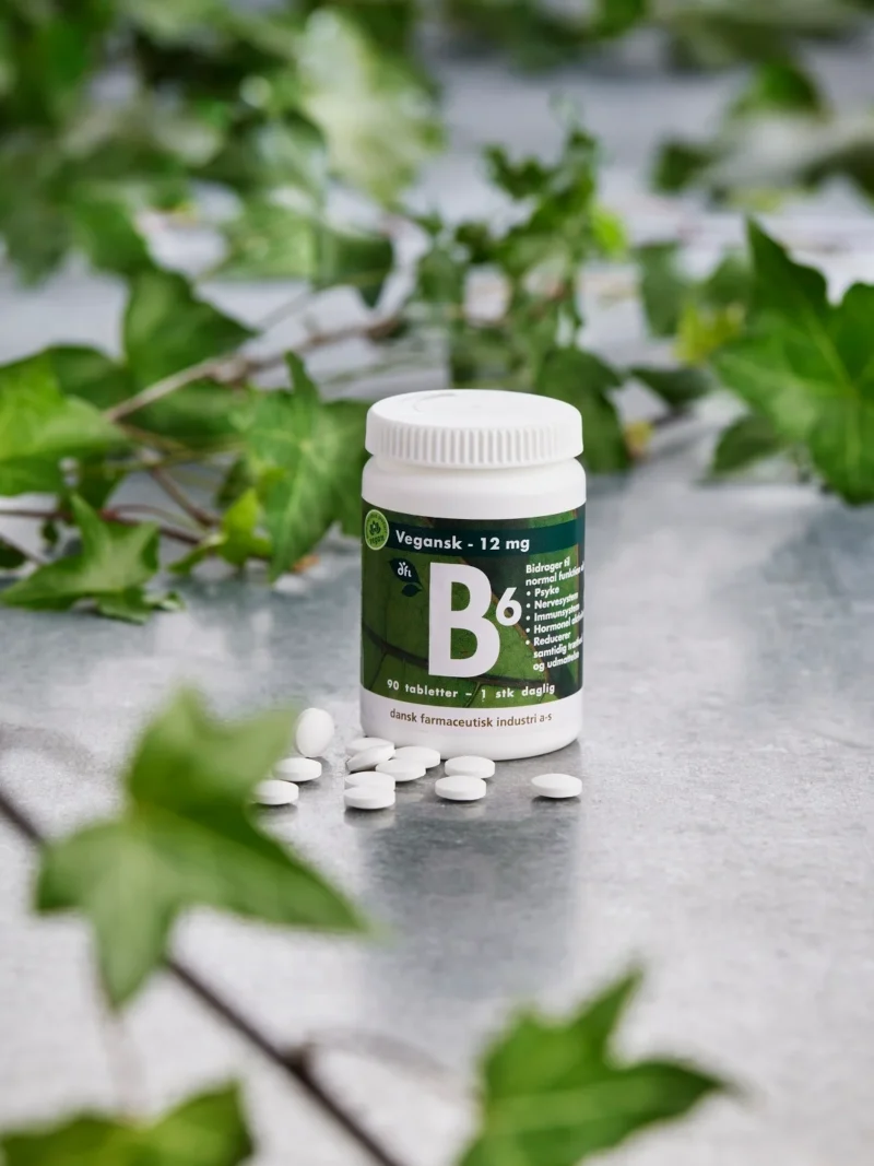 Dose mit Vitamin-B6-Tabletten, weiße Tabletten davor verstreut und grüne Blätter im Hintergrund
