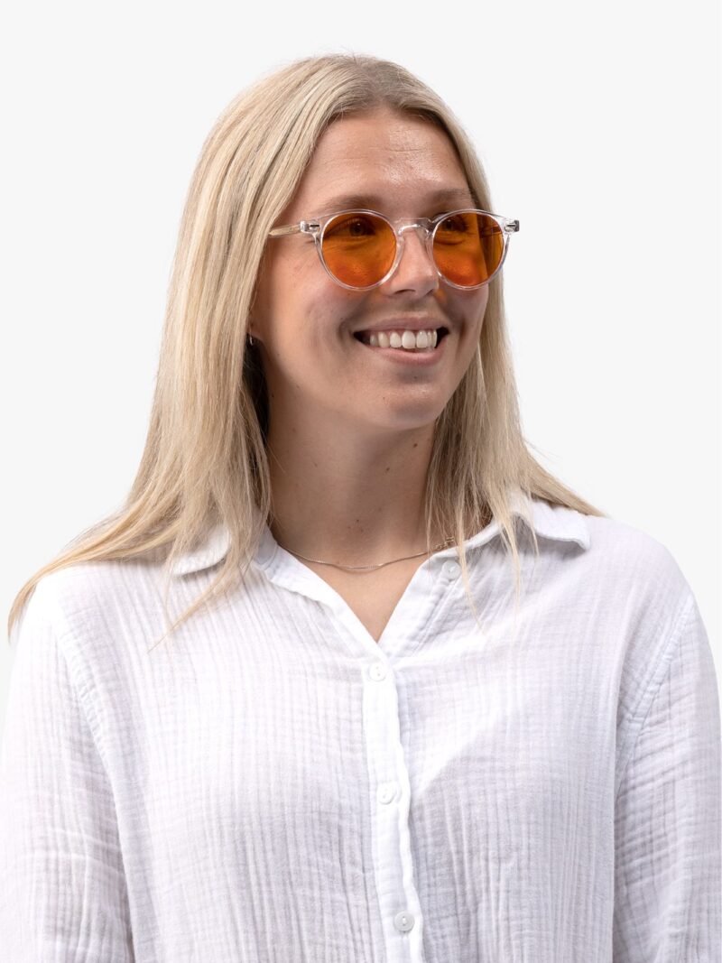 Lächelnde Frau mit langem blondem Haar, transparenter Brille mit orangefarbenen Gläsern und weißer Hemdbluse