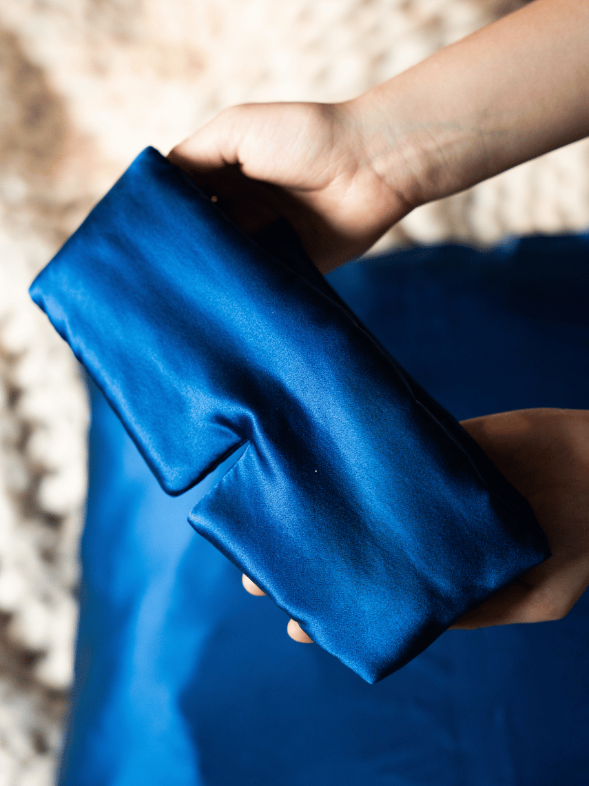 Hände halten glänzende blaue Seiden-Schlafmaske auf blauem Stoff