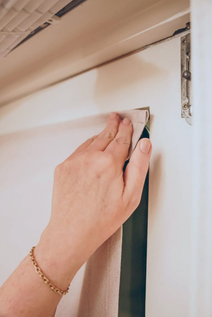 Hand befestigt Vorhang am Fensterrahmen, goldenes Armband sichtbar